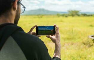 Close up of man hands taking photos of a landscape with the cell phone. Rear view of a person taking a photo of a field with his cell phone, rear view of a man taking photos of a field