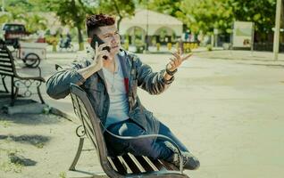 Man sitting on a bench calling on the phone, young man sitting on a bench with cell phone, close up of a young man calling on the phone sitting on a bench photo