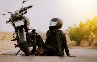 motociclista sentado siguiente a su motocicleta. motociclista sentado y propensión en su motocicleta en el asfalto foto