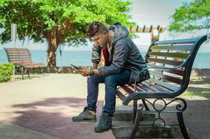 man sitting on a bench checking his phone, young man checking his cell phone sitting on a bench photo