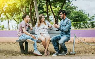 Three happy friends talking in a park. Three teenage friends talking sitting on a park bench, Group of three friends talking sitting in a park. Concept of people talking in the park photo