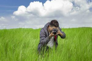 hombre tomando imagen con cámara en el campo, fotógrafo en el campo tomando un imagen, latino hombre en un verde campo tomando un imagen foto