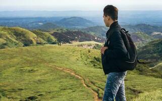 closeup of a backpacker watching a hill, adventurous man watching a hill with background horses on the hill, man with backpack on a hill photo