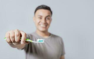 Smiling young man showing toothbrush with toothpaste isolated. Smiling people holding toothbrush with toothpaste with copy space, Smiling man showing a toothbrush in the foreground photo