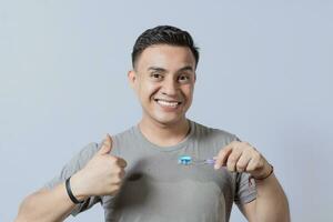 Smiling handsome guy holding a toothbrush with thumb up. Smiling people holding toothbrush with thumbs up gesture, Young man holding a toothbrush with thumb up isolated photo