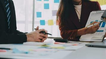 två kreativ företag människor möte och planera använda sig av posta den anteckningar klibbig notera på skrivbord till dela med sig aning, analys data Diagram och Graf med lagarbete strategi brainstorming i kontor. video