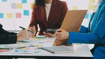 Two creative business people meeting and planning use post it notes sticky note on desk to share idea, Analysis data chart and graph with teamwork strategy brainstorming in office. video