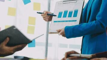 två kreativ företag människor möte och planera använda sig av posta den anteckningar klibbig notera på skrivbord till dela med sig aning, analys data Diagram och Graf med lagarbete strategi brainstorming i kontor. video