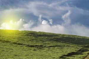 Image of a hill surrounded by other green hills, A path to a green hill with blue sky with copy space photo