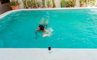 Young man swimming in a tropical hotel pool. Handsome man on vacation swimming in a hotel pool, Man on vacation swimming in a blue swimming pool photo