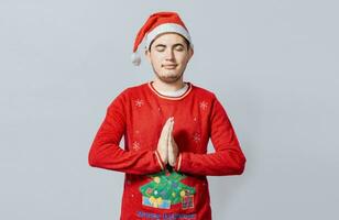 Guy with hands together praying in christmas isolated, concept of person with christmas hat praying and making a wish. Man with christmas hat with praying hands isolated photo