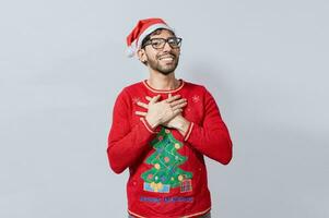 Thankful people in christmas clothes smiling with hands on chest. Man in christmas hat with sincere lovely smile feeling thankful, Smiling guy in christmas hat making thank you gesture photo