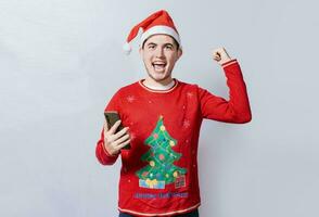 Happy smiling man in christmas hat holding cellphone celebrating, Happy guy in christmas hat holding cellphone celebrating, Teenager in christmas hat celebrating a promotion with the cell phone photo