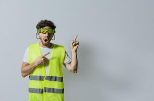 Surprised builder worker pointing finger to the right isolated. Construction worker with vest surprised pointing an advertisement to the side. Builder engineer pointing finger to the right isolated photo