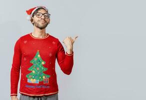 Friendly Christmas man pointing to a space to the side. Friendly smiling young man in christmas clothes pointing at a promo. Cheerful christmas man concept pointing promo offer isolated photo