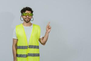 Construction worker with vest surprised pointing an advertisement to the side. Builder worker pointing finger to the right isolated. Builder engineer pointing finger to the right isolated photo