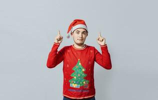 Guy in Christmas clothes pointing and recommending. Portrait of guy in sweater and christmas hat pointing up isolated. Caucasian young man in Christmas clothes pointing up an advertisement photo