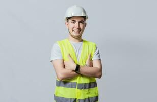 Portrait of smiling handsome engineer on white background, Portrait of young engineer wearing helmet and vest isolated. Young smiling engineer wearing helmet and vest with crossed arms isolated photo