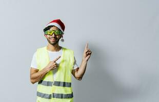 Construction worker with christmas hat pointing to an advertisement. Builder worker with christmas hat pointing a finger at a promotion. Builder engineer in christmas hat pointing to the right photo