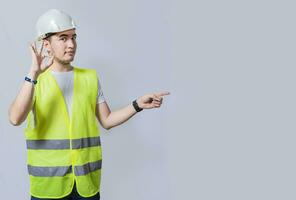 Handsome engineer recommending a product on white background, Young engineer pointing and recommending a product isolated. Builder engineer presenting a product with ok gesture photo