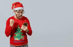 Excited guy in christmas hat looking at cellphone and celebrating. People in santa hat looking at cell phone excited, Excited young man in christmas hat using cellphone celebrating photo