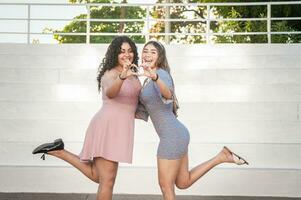 Close up of two girls making a heart shape, two friends together forming a heart, love hands sign photo