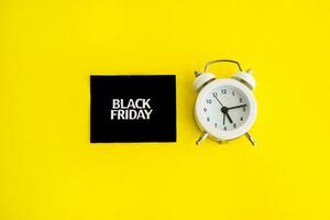 white alarm clock and an inscription on a black square - black Friday on a yellow background. The topic of sales. photo