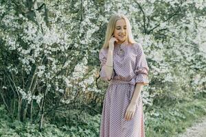 Blonde girl on a spring walk in the garden with cherry blossoms. Female portrait, close-up. A girl in a pink polka dot dress. photo