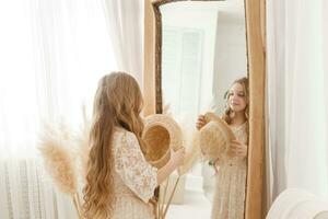 A beautiful teenage girl with long hair measures a straw hat in front of a mirror. Self-admiration of a blonde. photo