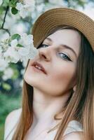 Beautiful young girl in white dress and hat in blooming Apple orchard. Blooming Apple trees with white flowers. photo