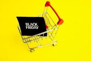 Shopping cart, and a black square that says black Friday on a yellow background. The topic of sales. photo