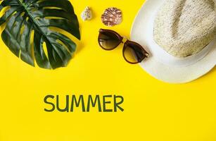 Beach accessories on the yellow background - sunglasses and striped hat. Summer is coming concept.Tropical leaves Monstera. Summer flat lay, top view. Text Summer. photo