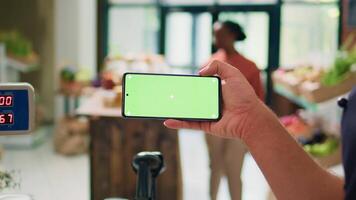 Seller showing greenscreen on phone display, presenting isolated mockup template on gadget in local organic zero waste store. Young man vendor using blank chromakey copyspace screen. video