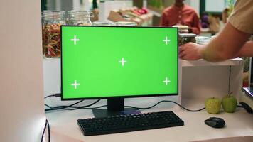 Seller at register uses greenscreen on computer, showing isolated copyspace display on pc monitor. Young man small business owner encourages healthy lifestyle with blank chromakey. video