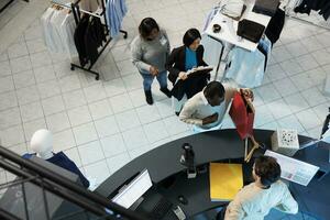 Diverse people waiting in line to pay for selected clothes at department mall checkout desk top view. African american man taking shopping bag from cashier at store cash register photo