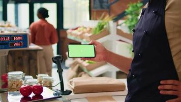 Merchant with phone greenscreen at store counter, presenting isolated chromakey display on mobile gadget. Farmer and vendor using modern copyspace template with mockup technology. video