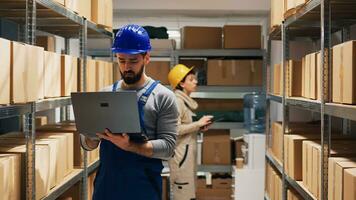 Depot supervisor working with laptop in storage room and checking logistics of merchandise on racks. Young man using inventory stock to arrange cargo goods in packages, industrial job. photo