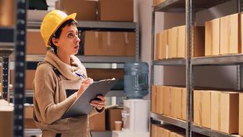 Female employee checking list of products in depot, working on stock logistics with papers and counting packages on racks. Storage room manager examining cardboard boxes for shipment. photo