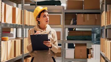 Young woman checking list of merchandise in depot, working on stock inventory and counting boxes on shelves. Warehouse supervisor examining cardboard packages for distribution. photo