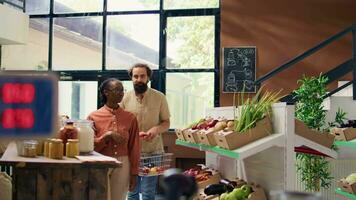 Couple asking seller about products in organic natural supermarket, vendor in apron offers produce samples locally grown. Young man encourages bio sustainable healthy eating. video