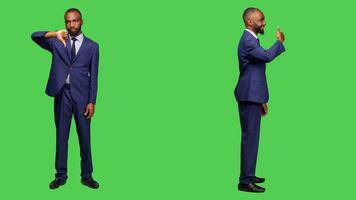 Businessman giving thumbs down and thumbs up posing full body green screen backdrop, showing approval and disapproval in studio. Young adult in suit expresing like and dislike. photo