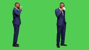 Company employee drinking coffee cup in studio, serving caffeine refreshment over full body greenscreen backdrop. Young manager enjoying refreshment drink, wearing formal suit on camera. photo