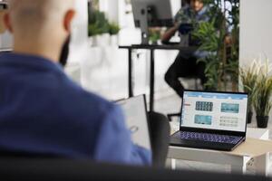 Businessman monitoring fund and stock exchange investments on laptop screen while working in business office. Executive manager studying market trends and financial data in coworking space photo