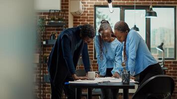 Women colleagues reading analytics files on office desk, reviewing official annual data reports on documents for business development. Team of people meeting in boardroom coworking space. photo