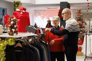 Old customers checking belts and ties in clothing store, looking at accessories to match formal attire for christmas eve dinner outfit. Senior couple searching for clothes during winter sales. photo