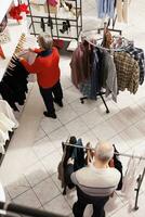 mayor personas hojeada para ropa en perchas y mirando para Perfecto formal atuendo a atender Navidad cena festividad. mayor Pareja haciendo compras juerga a centro comercial durante ventas estación. foto