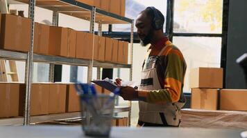 Male worker listening music in depot, working with merchandise stock in storage room. Warehouse manager checking inventory list on papers, planning quality control and distribution. photo