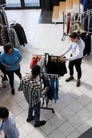 Top view of stylish people shopping for casual wear in modern boutique, buying clothes from new fashion collection. Diverse shoppers looking at hangers full with fashionable merchandise in store photo