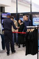 Security guard keeping waiting shopper crowd in check before stores open on Black Friday. Angry diverse people buyers standing behind control barrier with redtape in shopping mall during sales photo