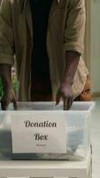 verticaal video klanten aan het doen humanitair hulp, doneren hun kleren in mode winkel naar helpen mensen in nodig hebben. klanten brengen hun kledingstukken naar kleding op te slaan, plaatsen hen in bijdrage doos
